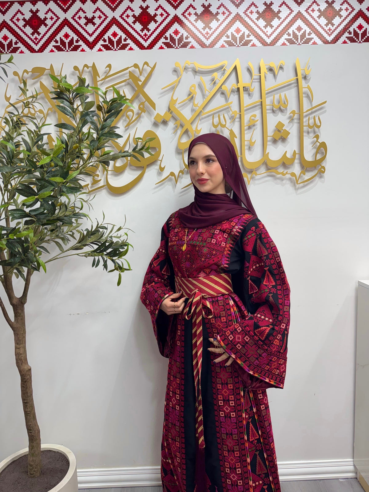 Model wearing a burgundy and black Palestinian thobe with detailed geometric embroidery